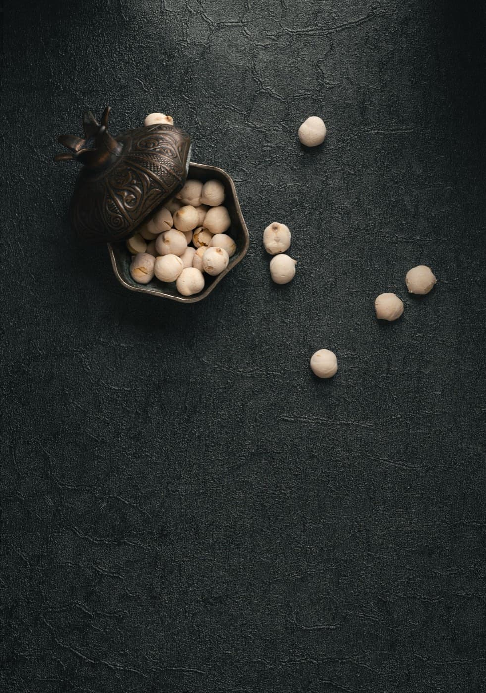An ornate bowl of raw, premium makhana (fox nuts) on a dark textured surface